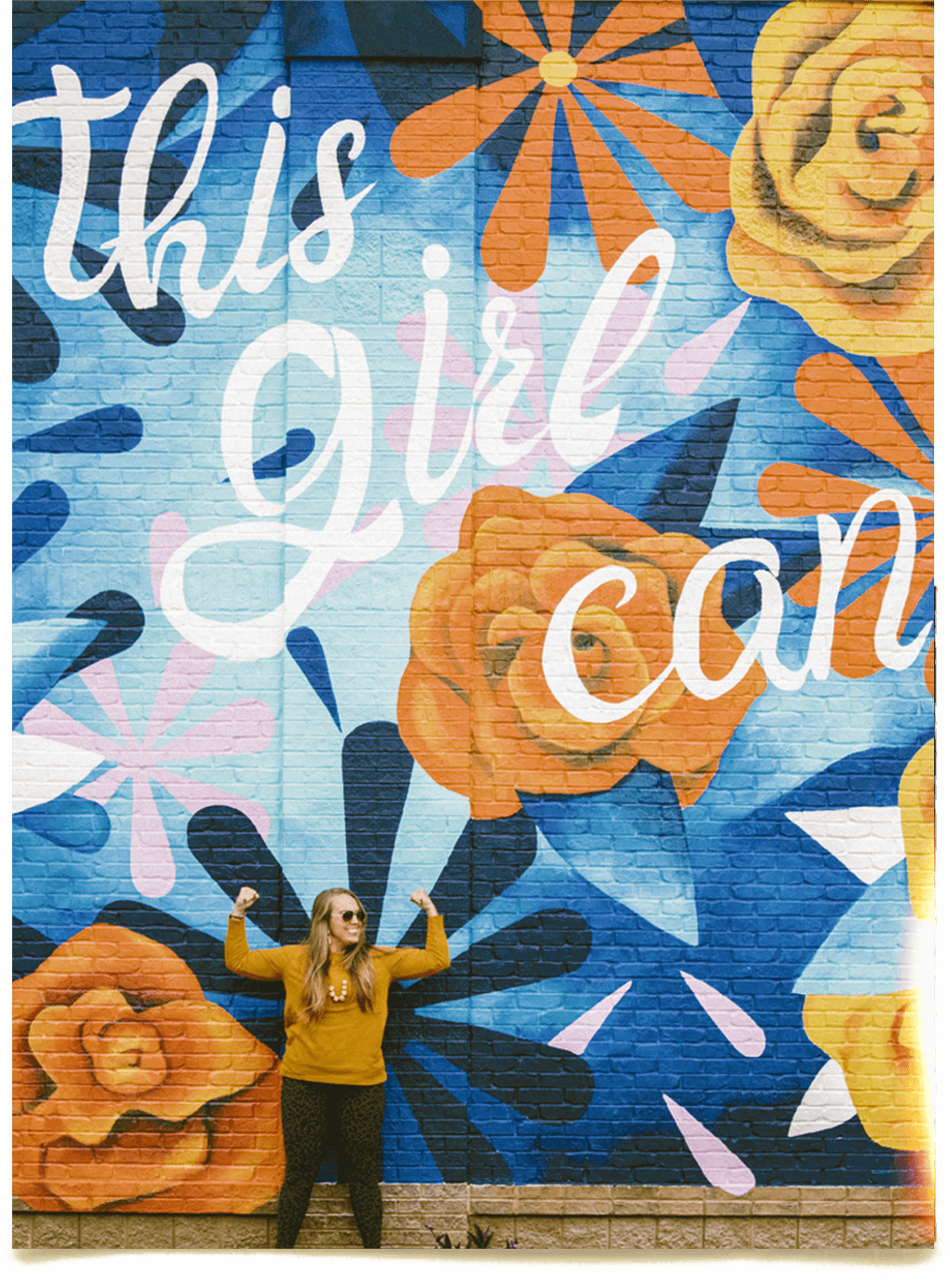 woman strong pose with art mural written this girl can