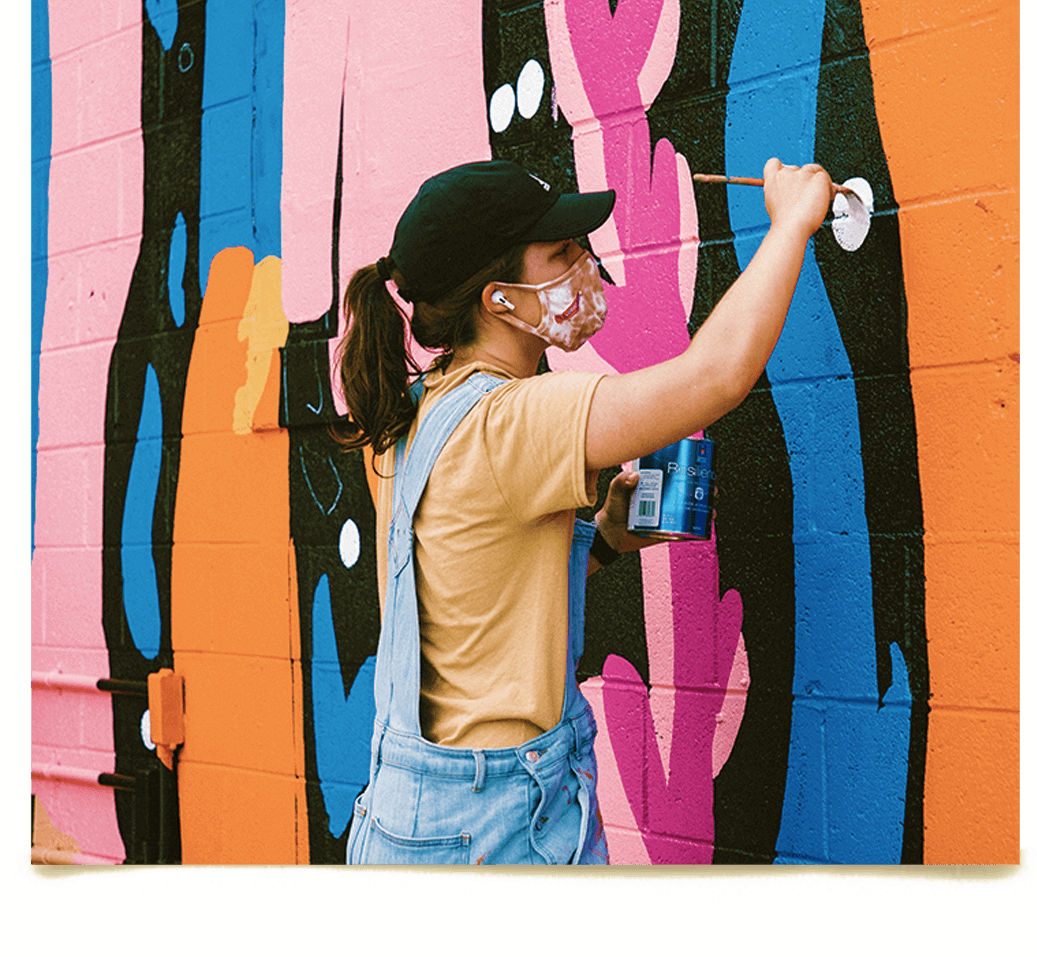 woman in overalls painting colorful wall