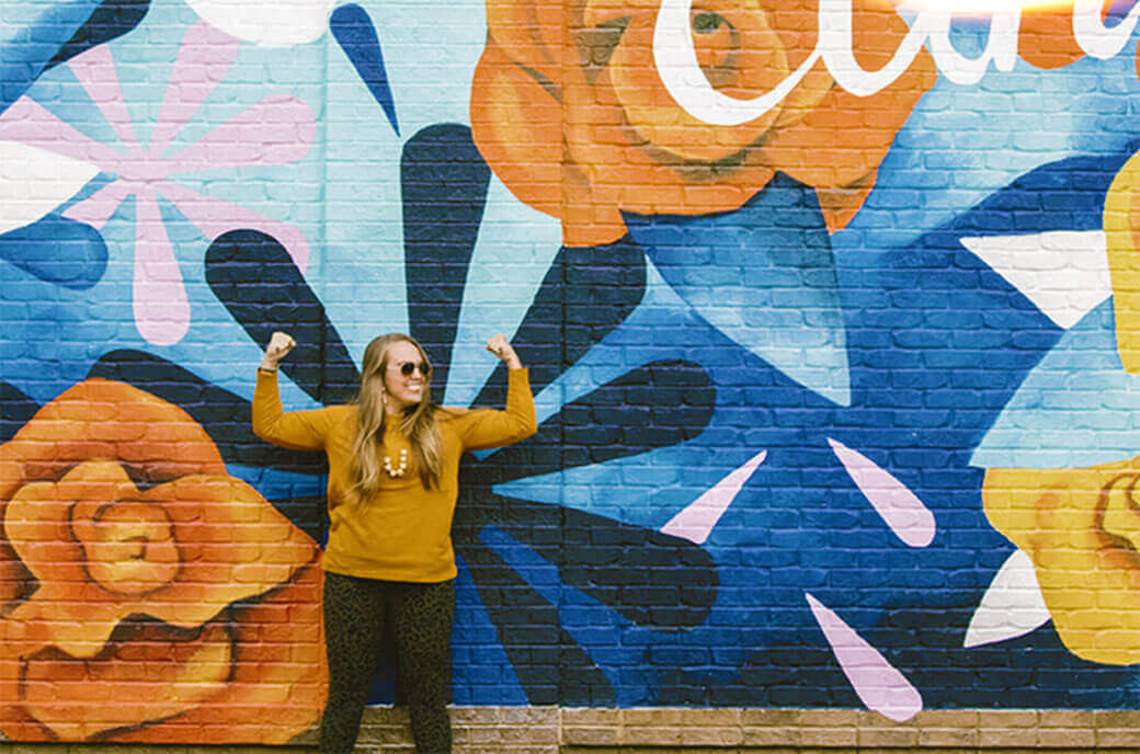 Woman strong pose in front of a colorful art mural 